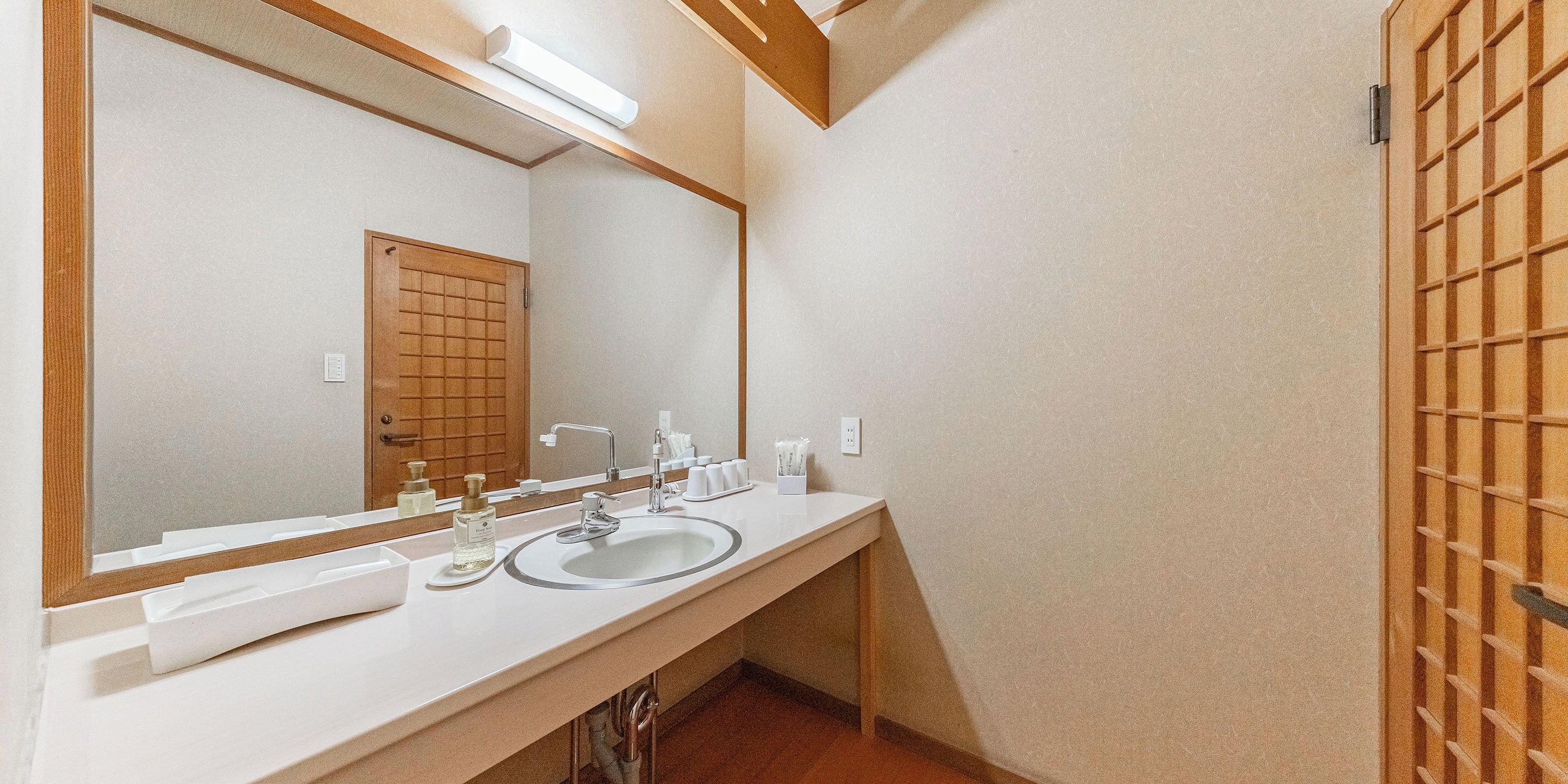 A bathroom with a large mirror, a sink, and a wooden door.