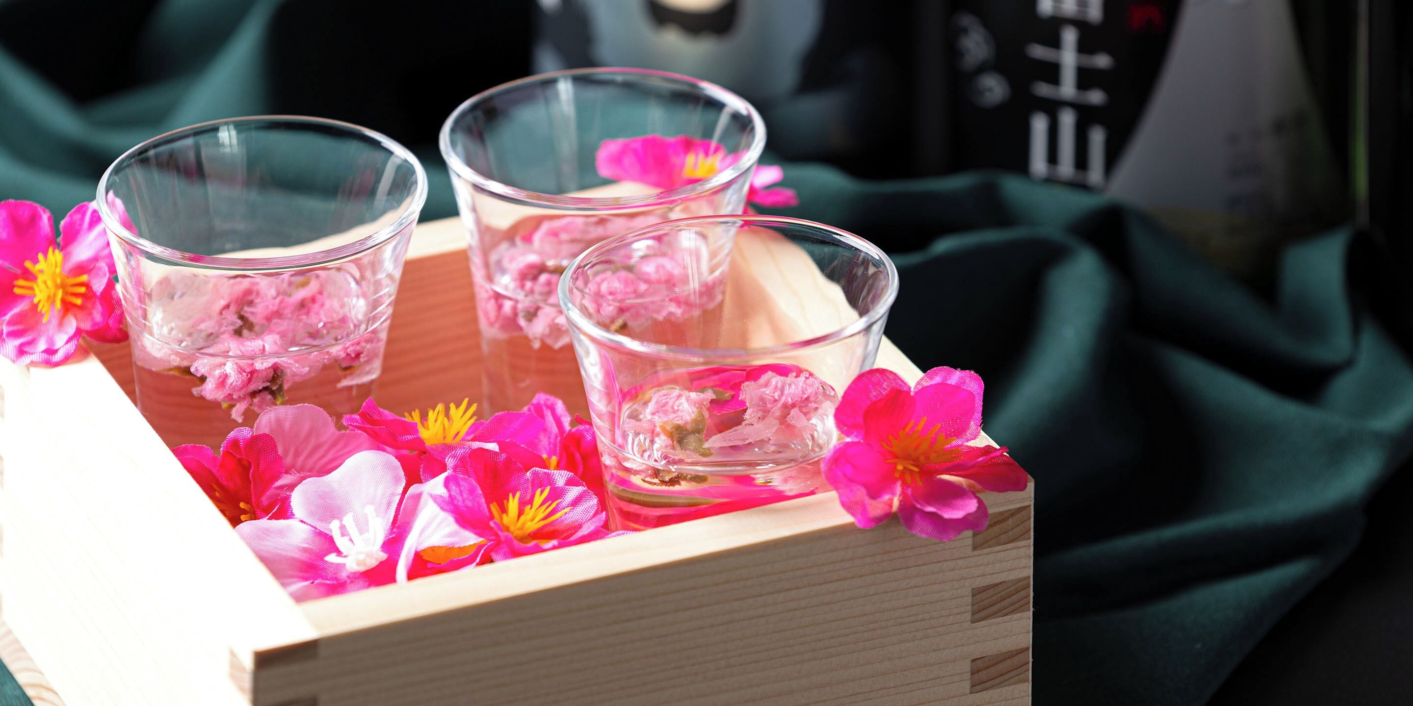 Tres vasos transparentes sobre una bandeja de madera con flores rosadas.