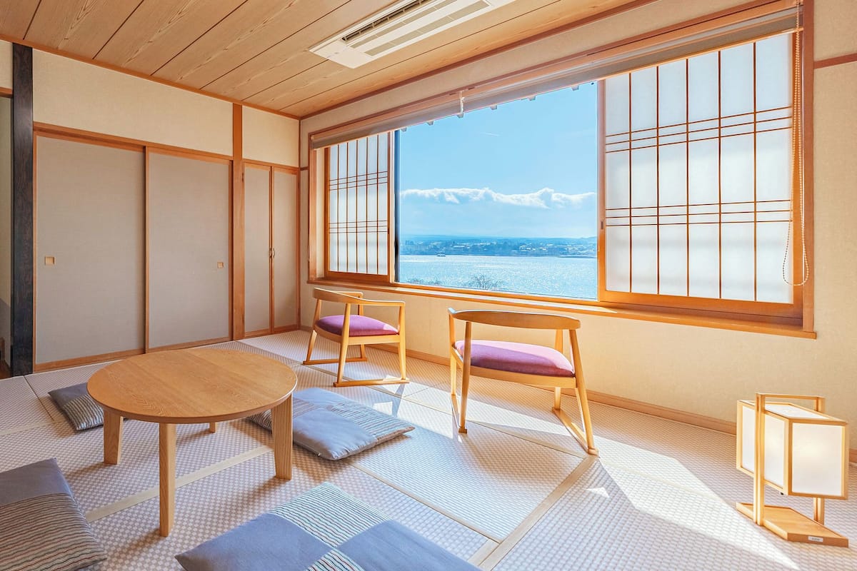 Une pièce avec un sol recouvert de tatamis, une table en bois, des chaises et une vue sur une montagne.