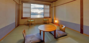 Una habitación con esterillas tatami, una mesa baja, dos sillas, un ventanal con biombos y una lámpara de pie.