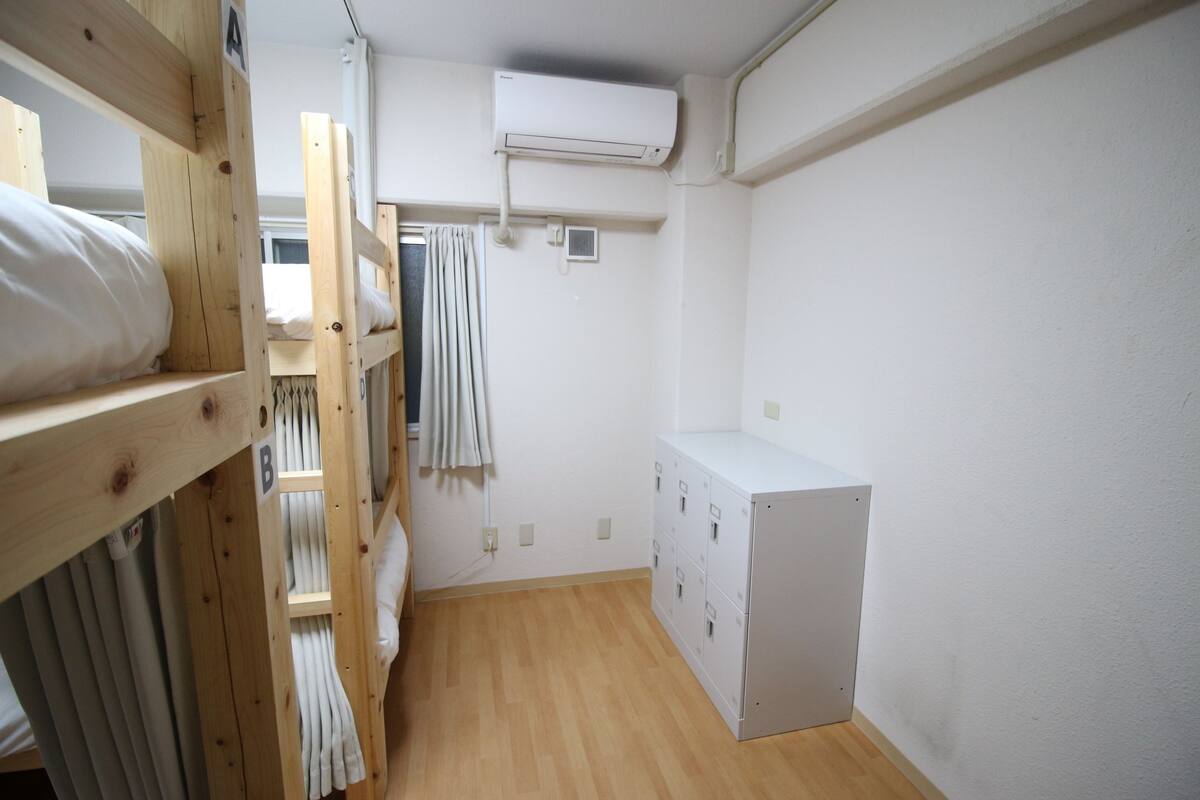 Una habitación pequeña y funcional con literas, un armario blanco y un equipo de aire acondicionado.