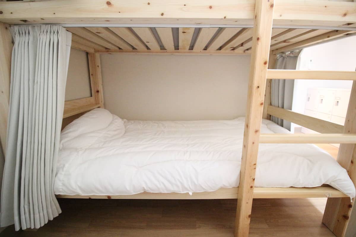 Una cama litera con ropa de cama blanca, estructura de madera y una cortina a la izquierda.