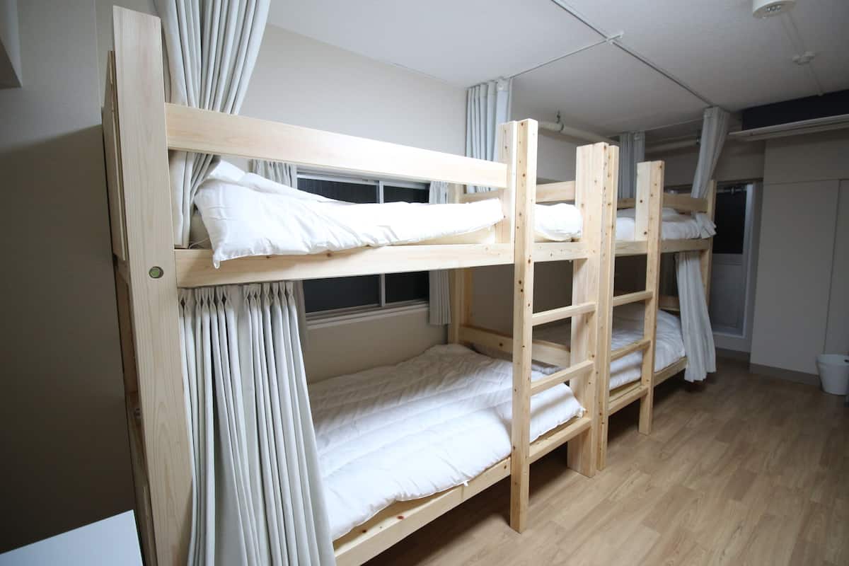 Dormitorio con literas de madera, ropa de cama blanca y ventana con cortinas.