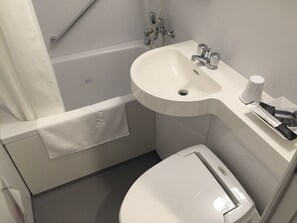 A modern bathroom with a bathtub, a sink, and a toilet. - Fukui Manten Hotel Ekimae (Fukui)