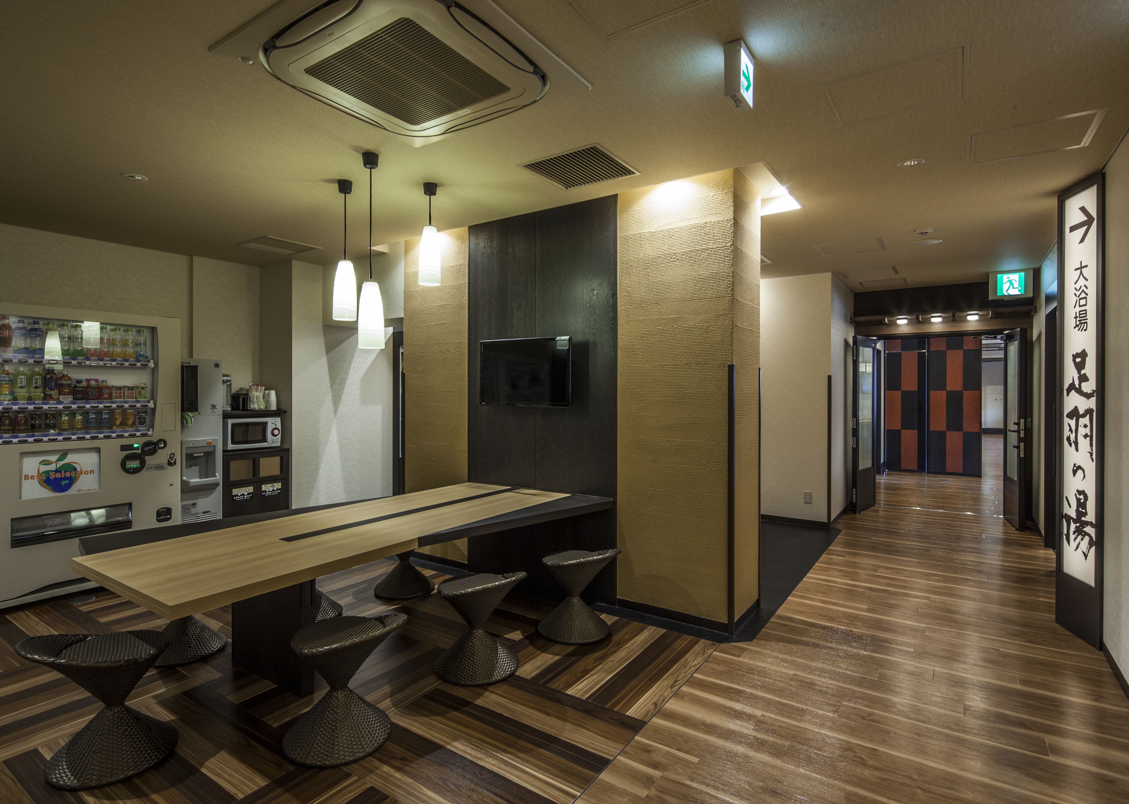 Een modern interieur met een lange houten tafel, meerdere krukken, een automaat en een televisie.