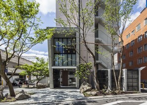 A modern building with large windows and a glass entrance, surrounded by trees and rocks. - Fukui Manten Hotel Ekimae (Fukui)