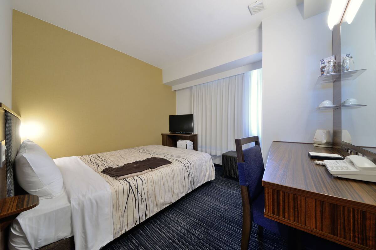 A hotel room with a bed, a desk, a chair, a television, and a window with curtains.