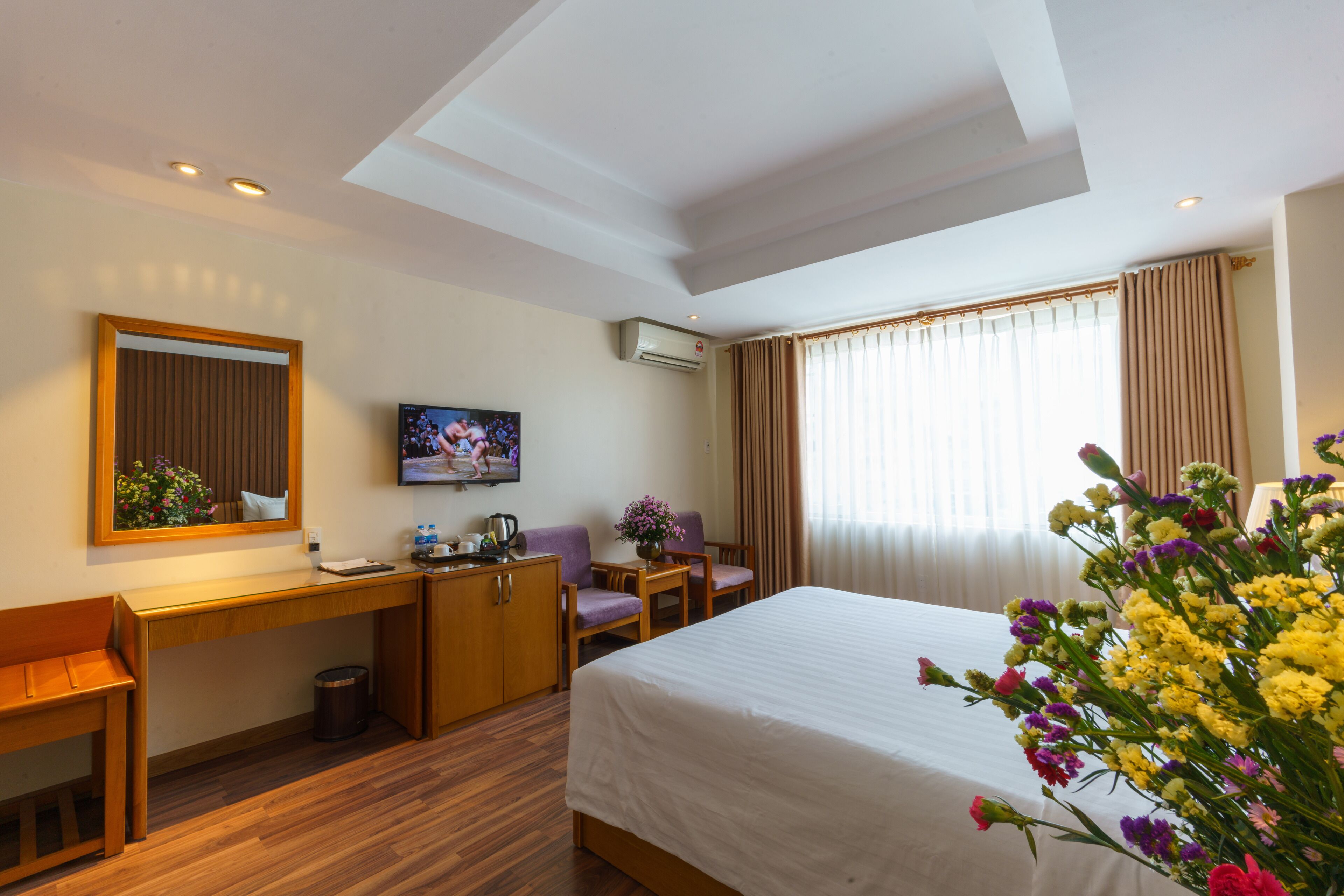 A hotel room with a bed, desk, chair, TV, and a large window with curtains.