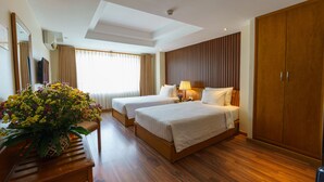A hotel room with two beds, a wooden wardrobe, a large mirror, and a potted plant.