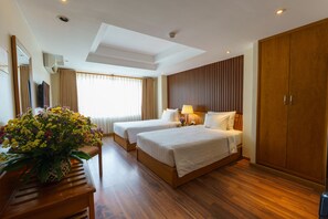 A hotel room with two beds, a wooden wardrobe, a large mirror, and a potted plant.