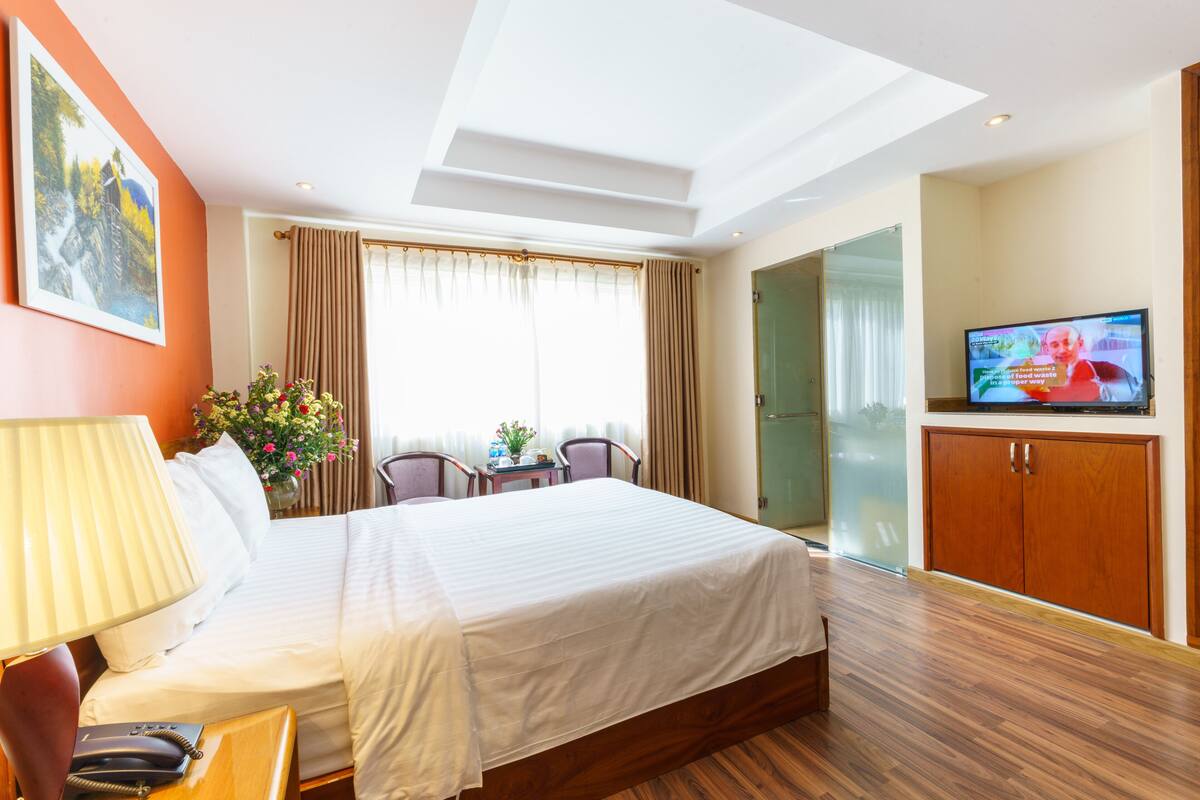 A hotel room with a large bed, a desk with a lamp, a TV, and a view of the outdoors.