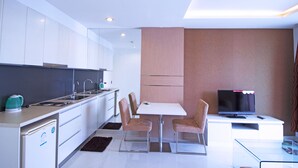 Une cuisine moderne avec des meubles blancs, un coin repas comprenant une table et des chaises, un téléviseur et un petit réfrigérateur.