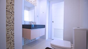 Une salle de bain moderne avec un sol carrelé, des toilettes blanches, un lavabo doté d’un plan de travail noir et un miroir au-dessus du lavabo.