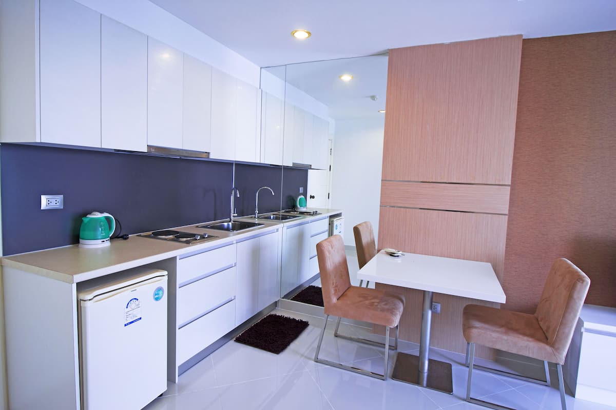 Una cocina moderna con armarios blancos, un refrigerador pequeño, un lavamanos y una zona de comedor con dos sillas y una mesa.