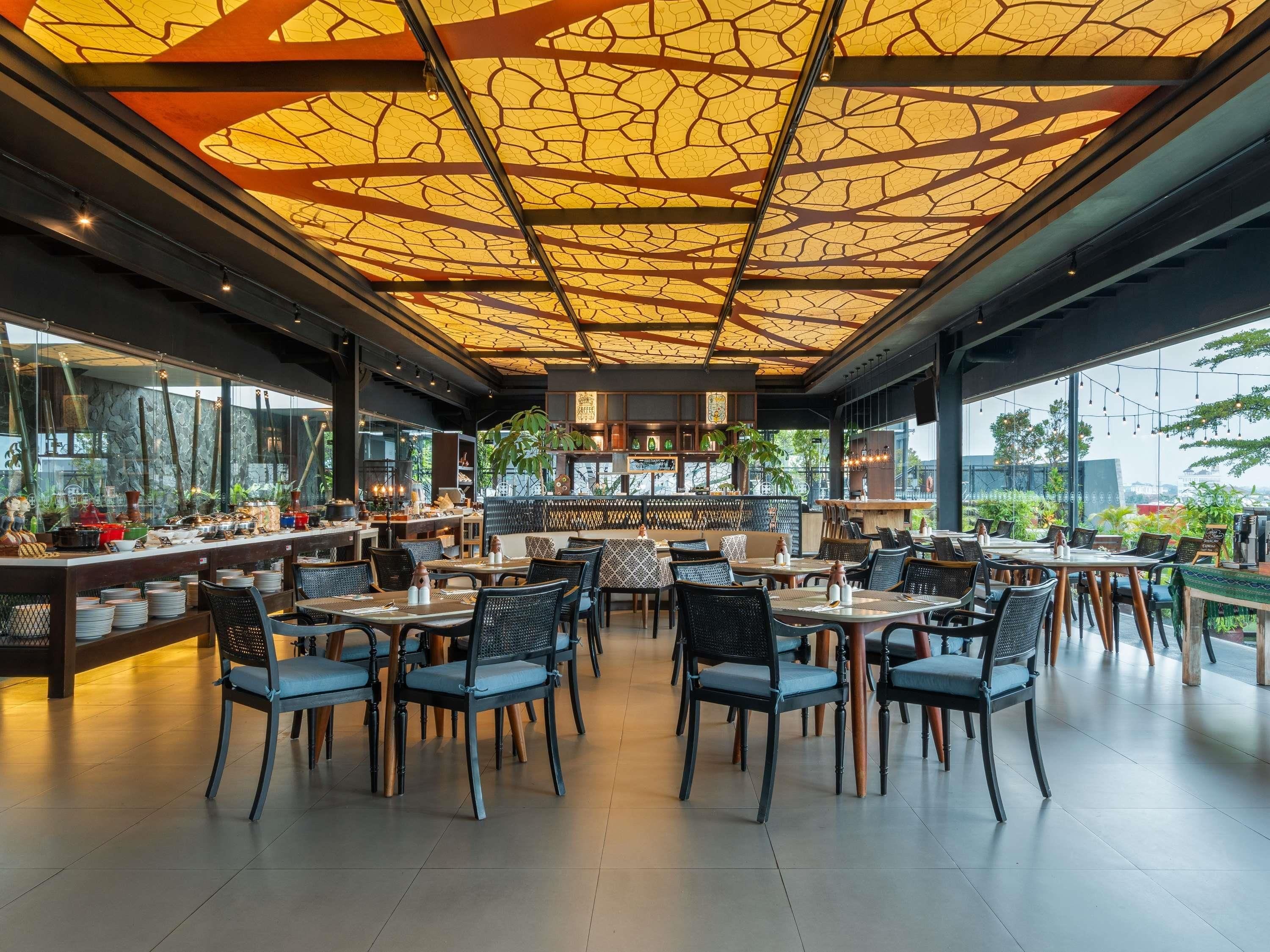 A restaurant with a modern interior, featuring a unique ceiling design, outdoor seating, and a view of the cityscape.