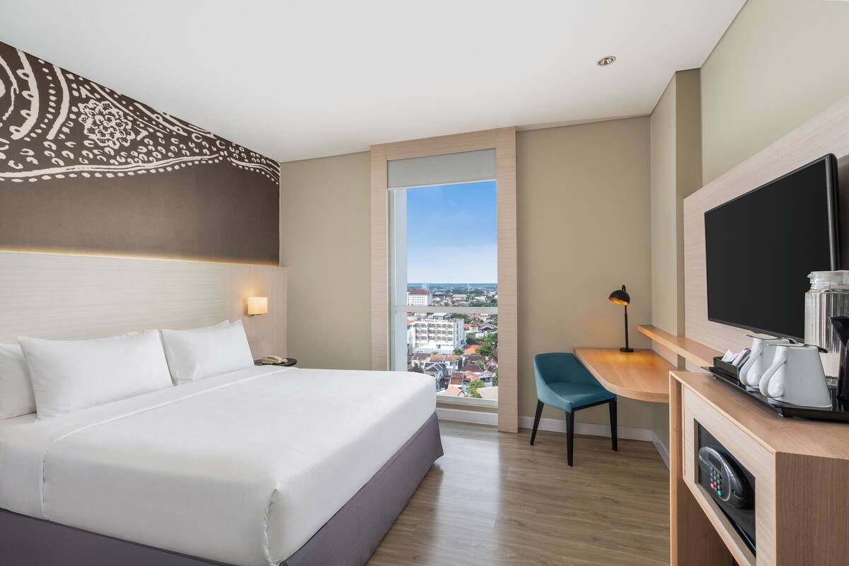 Una habitación de hotel con una cama grande, un escritorio con silla, televisor y cafetera.