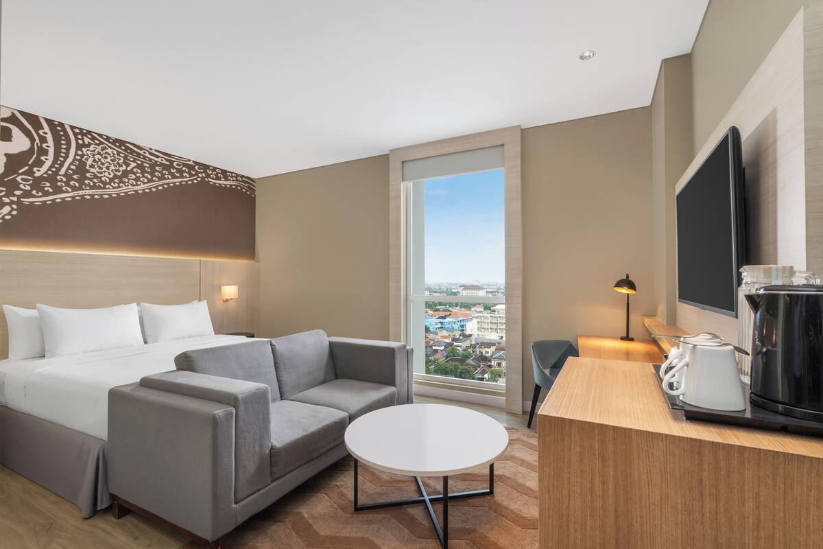 Una habitación de hotel con una cama, un sofá, una mesita, un televisor y una cafetera.