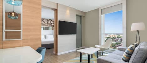 Una sala de estar moderna con una televisión de pantalla plana, un sofá, una mesa de comedor y vistas a la ciudad.