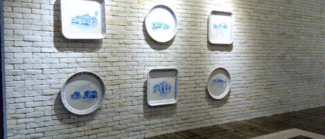 Un mur orné de nombreuses assiettes en céramique, de forme carrée ou ronde, décorées de motifs bleus, et fixées sur un mur en briques blanches.