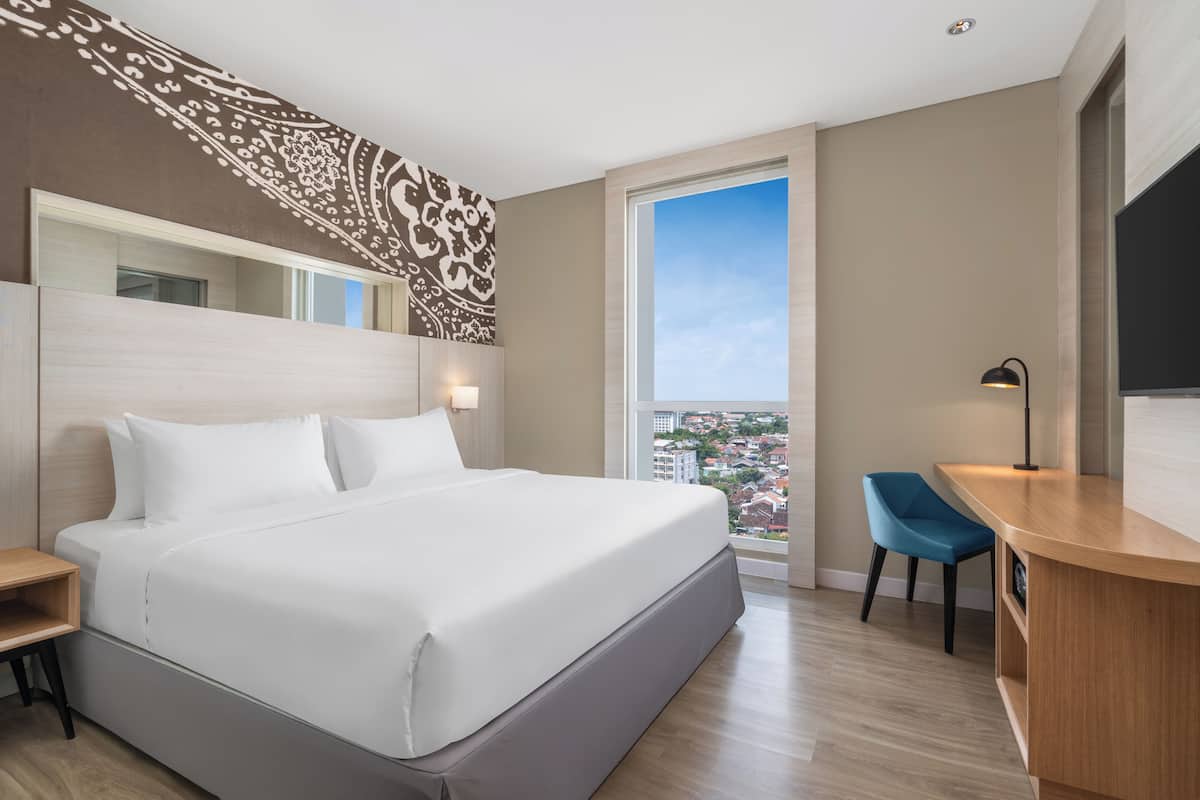 Una habitación de hotel moderna con una cama grande, un escritorio, una silla y un ventanal con vistas a la ciudad.