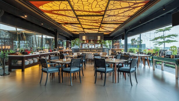 Un restaurante moderno con techo alto que presenta un diseño geométrico, ventanas amplias que ofrecen vistas al exterior y diversas opciones de asientos.