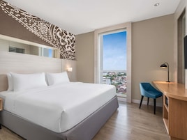 A hotel room with a large bed, a desk with a chair, a TV, and a window with a city view.