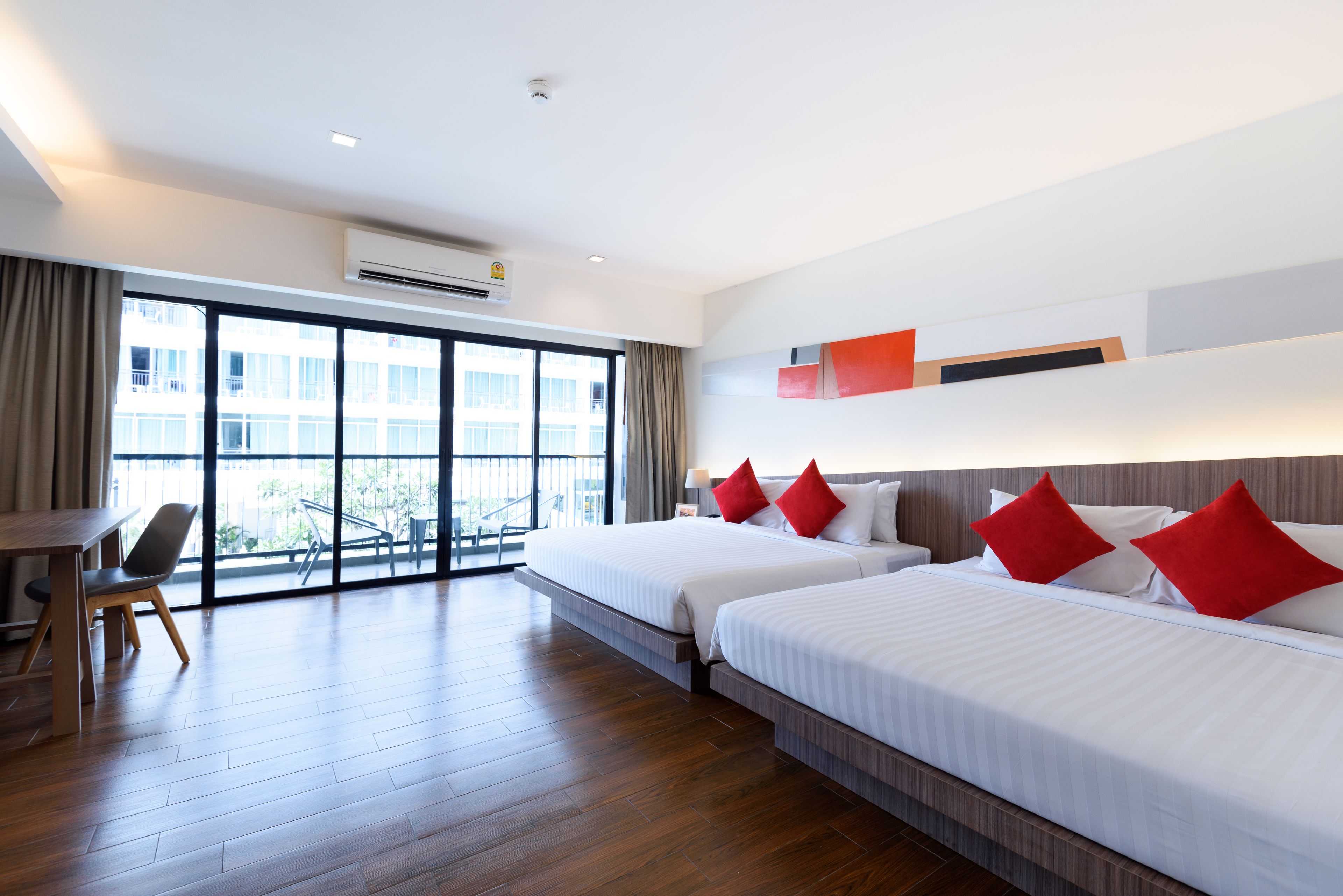 A hotel room with two beds, a desk, and a large window with a view of buildings.