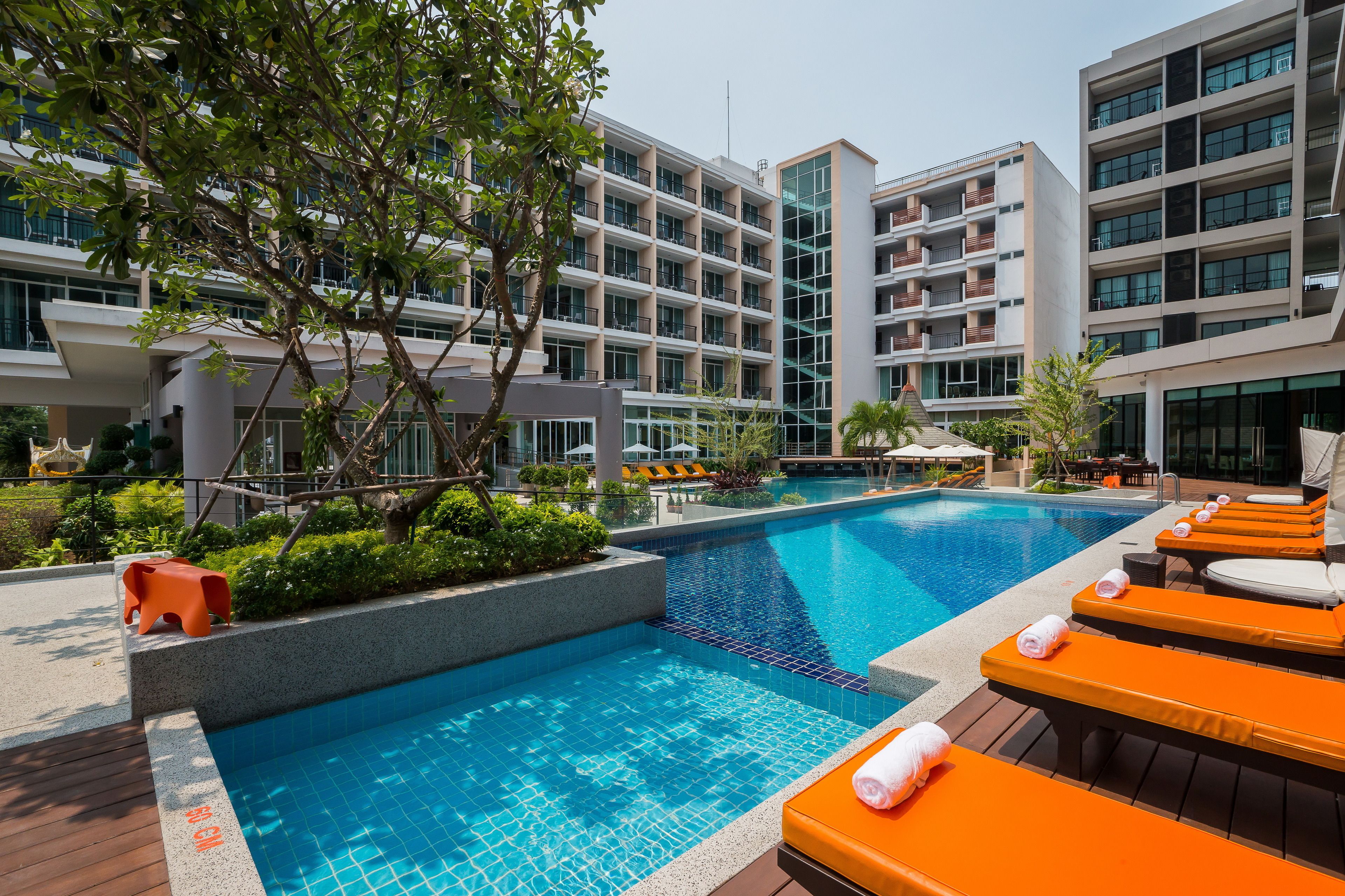 A modern hotel with a swimming pool, lounge areas, and a multi-story building with balconies.