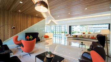 Un hall d’entrée moderne avec un plafond en bois, des murs en verre et un espace détente comprenant des fauteuils et un canapé orange.