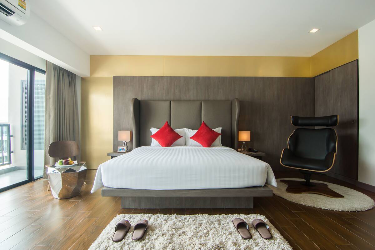 A modern hotel room with a large bed, a side table with fruit, a chair, and a view of the city.