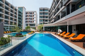Ein modernes Hotel mit einem zentral gelegenen Schwimmbad, mehreren Balkonen und Liegestühlen.