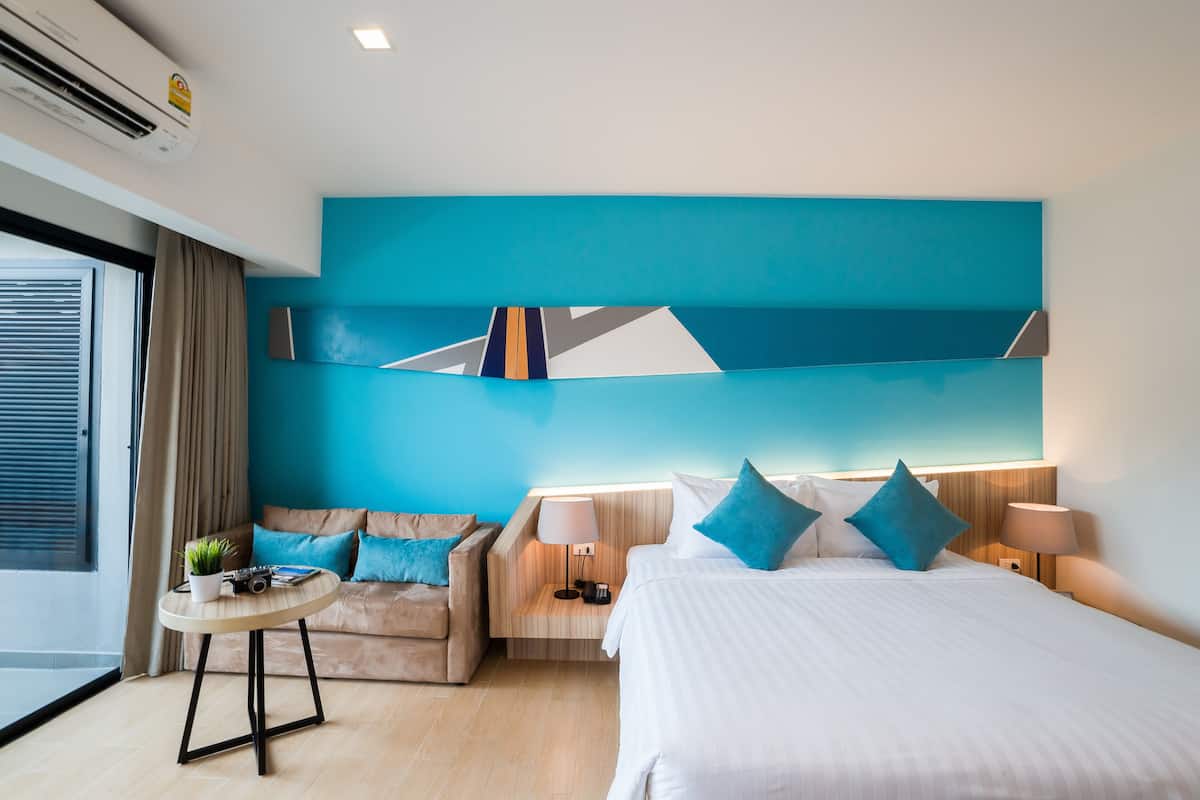 A modern hotel room with a large bed, a sofa, a small table, and a wall-mounted artwork.