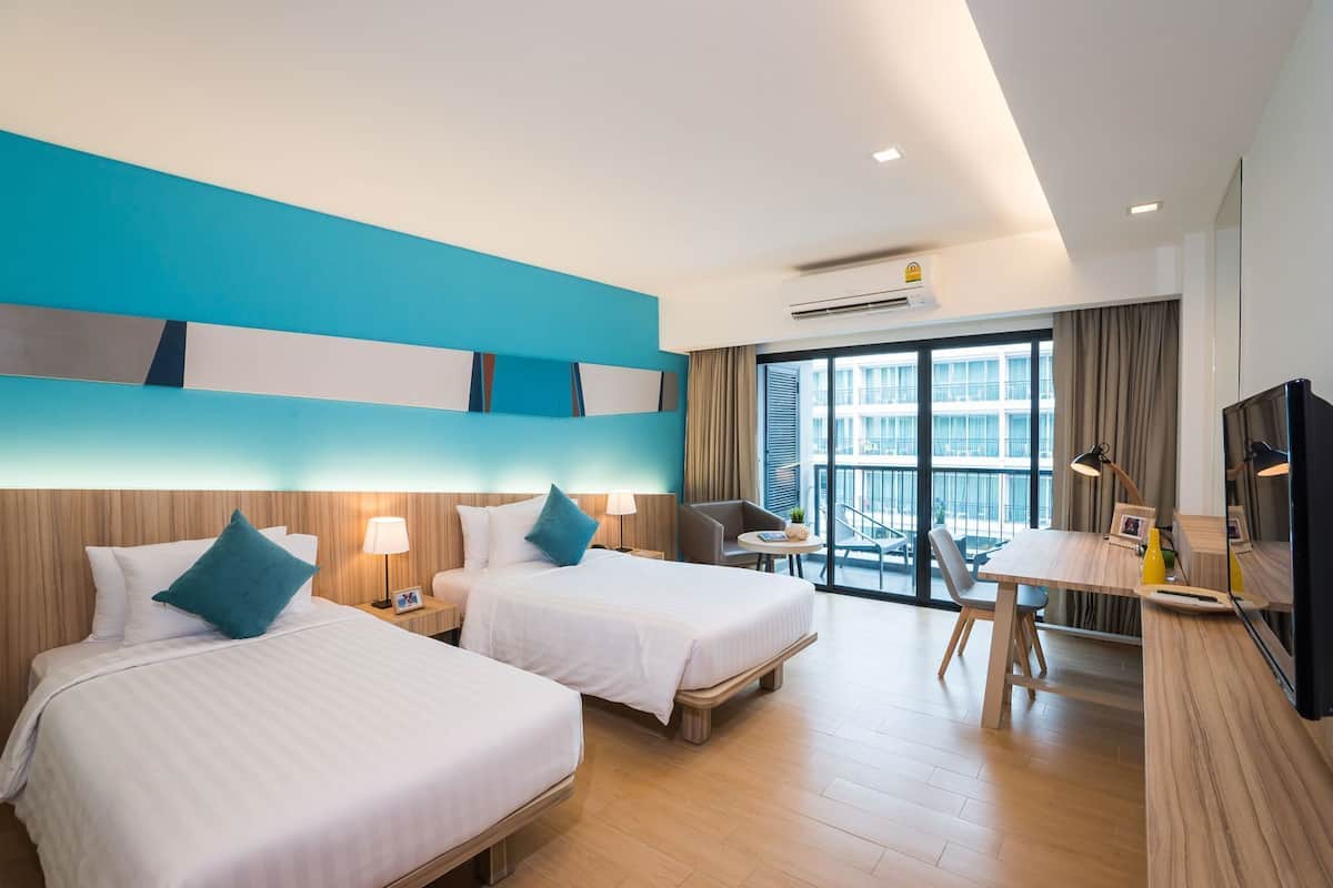 A hotel room with two beds, a desk, a chair, a TV, and a balcony with a view of the city.