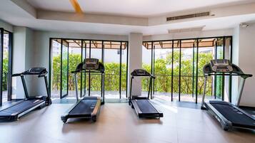 Ein Fitnessraum mit vier nebeneinander angeordneten Laufbändern, großen Fenstern mit Blick auf Grünflächen und einem modernen Deckenstil.