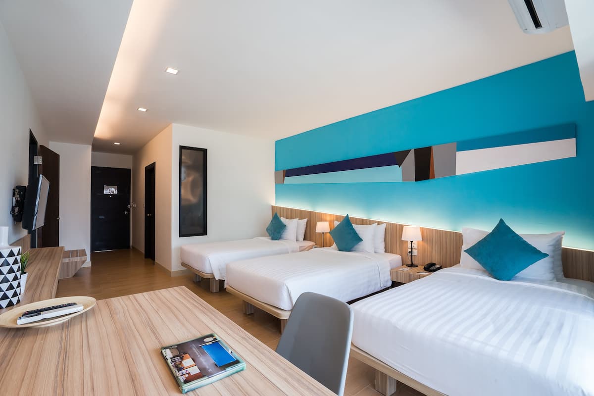 A hotel room with three beds, a wooden desk, and a modern wall design.