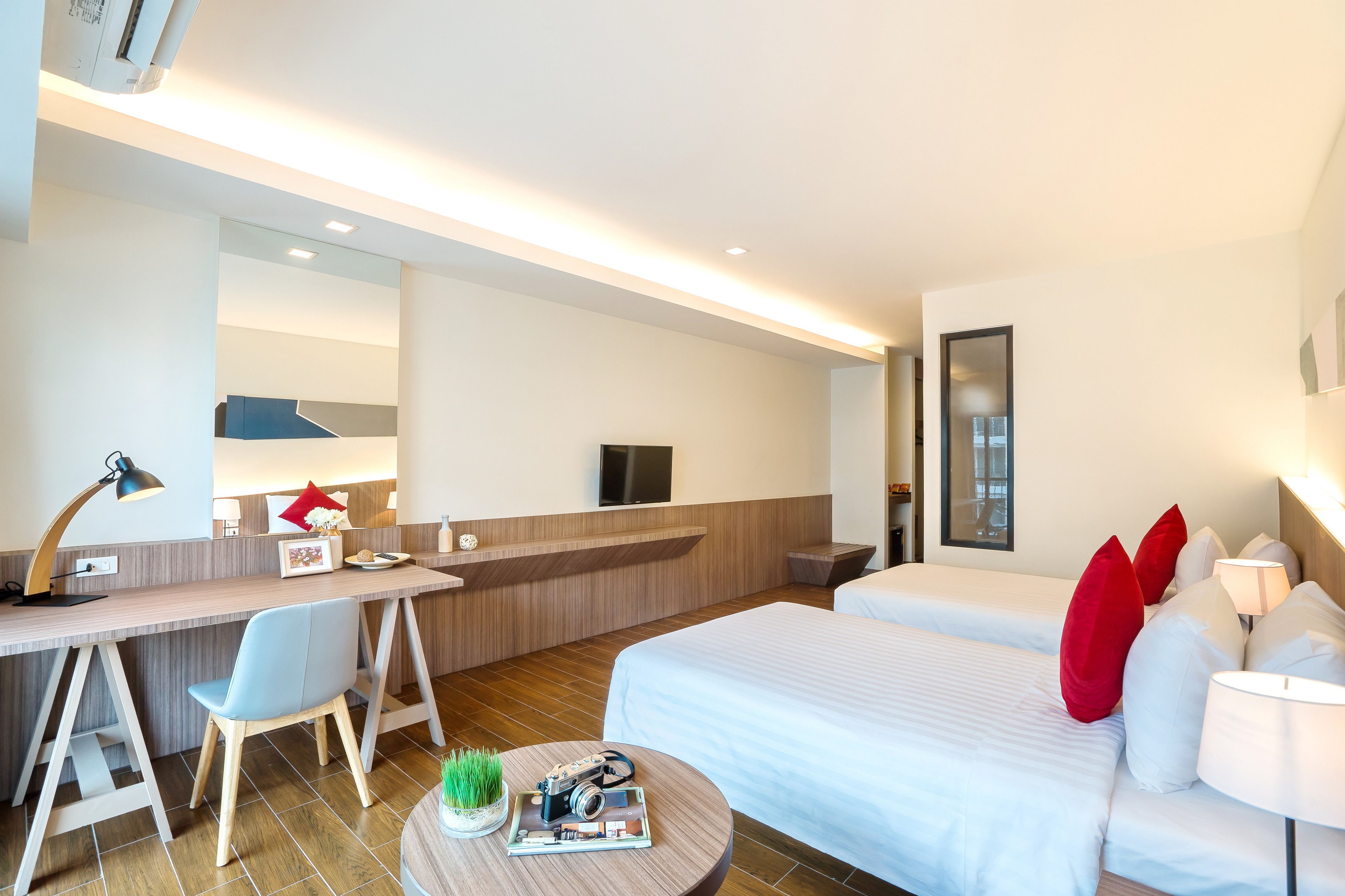 Ein modernes Hotelzimmer mit Schreibtisch, zwei Betten, Fernseher und Spiegel.
