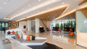 Eine geräumige Lobby im modernen Design mit einer großen Sitzecke, einer Treppe und einer Glaswand mit Blick ins Freie.