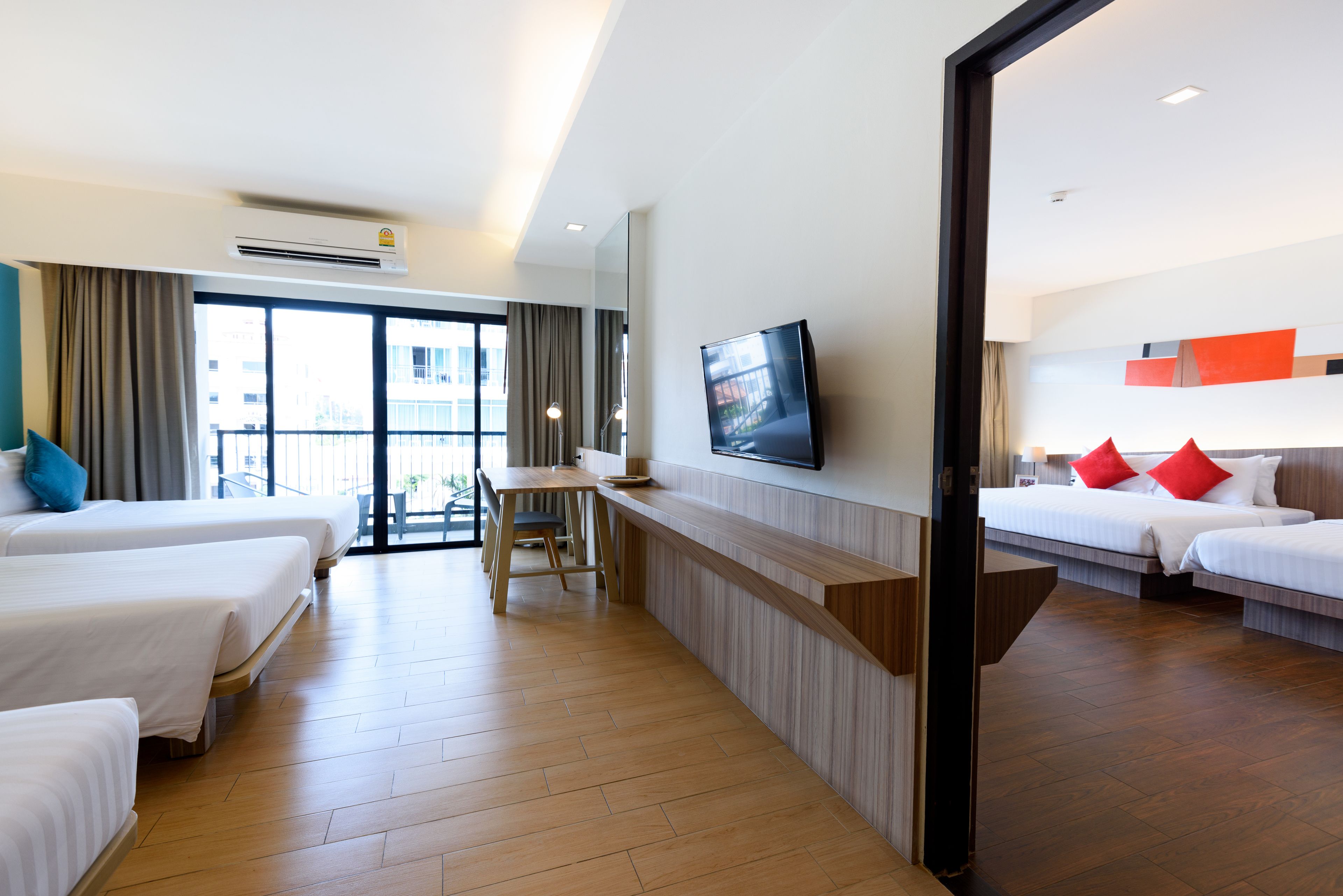 A hotel room with two beds, a desk, a TV, and a balcony with curtains.