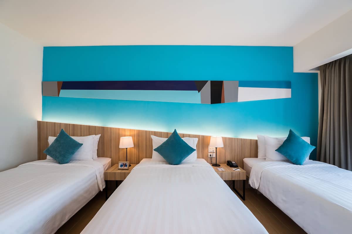 A hotel room with two beds, each with a blue pillow and white bedding. There are two bedside tables with lamps and a nightstand with a phone. The room has a modern design with a blue accent wall and wooden paneling.