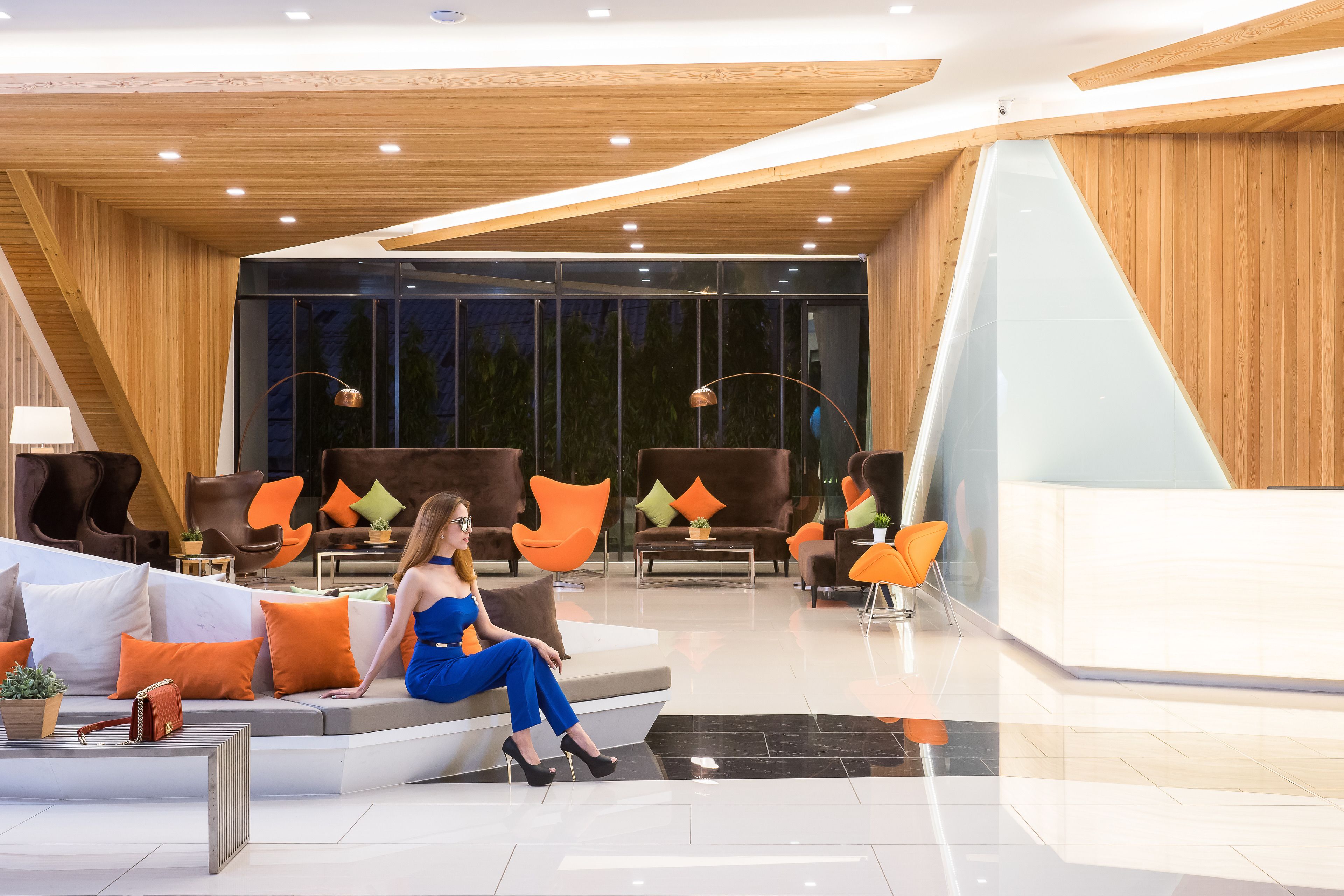 A modern lobby with a wooden ceiling, a reception desk, and seating areas with orange and brown chairs.
