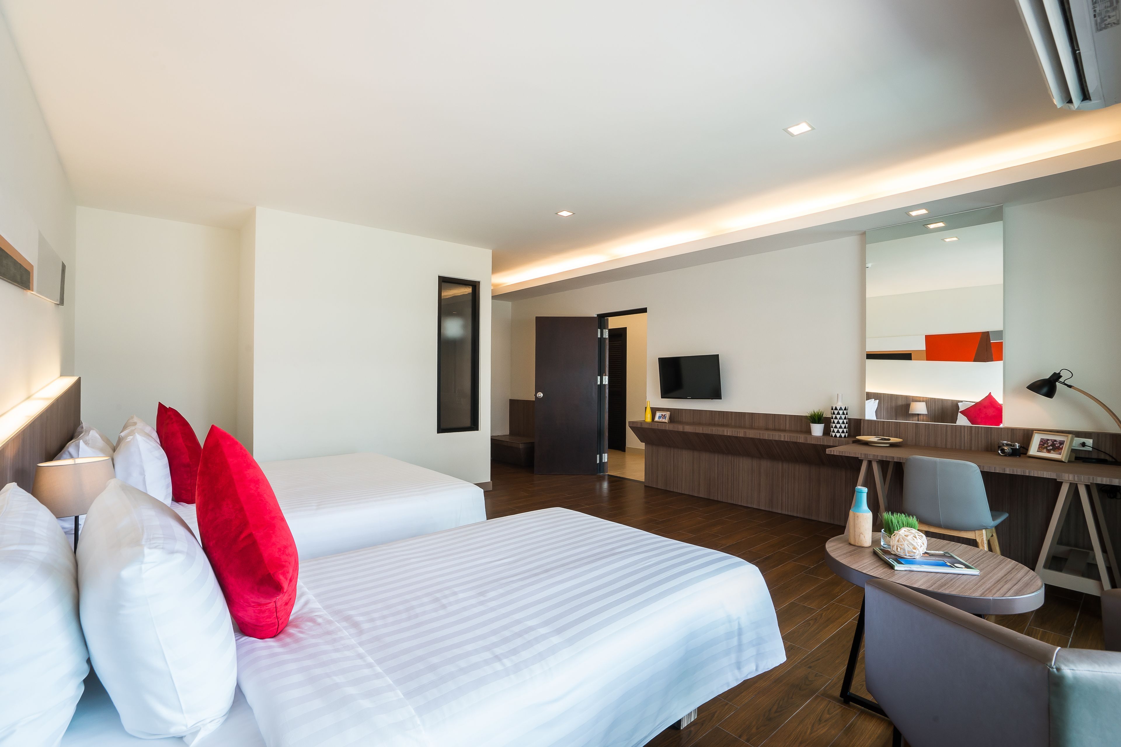 A hotel room with two beds, a desk, a chair, a TV, and a bathroom visible in the background.