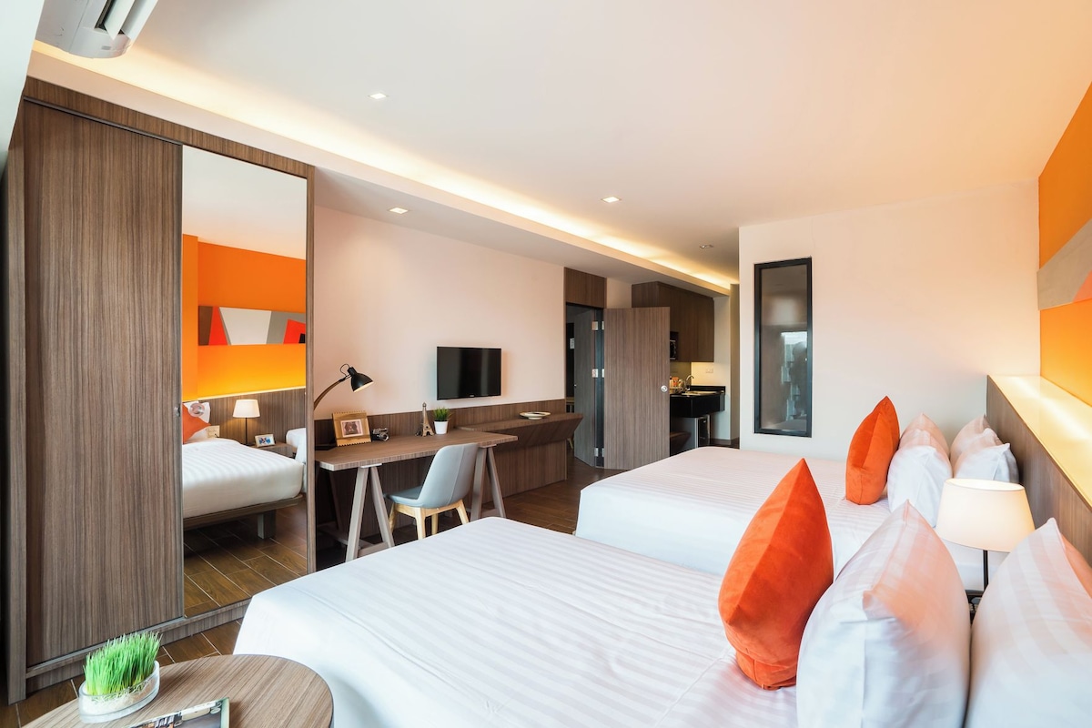 Ein Hotelzimmer mit zwei Betten, einem Schreibtisch, einem Fernseher und einem durch eine offene Tür einsehbaren Badezimmer.