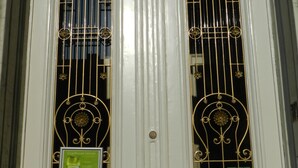 Une porte blanche dotée de deux fenêtres, chacune ornée de grilles métalliques décoratives et d’une enseigne verte.