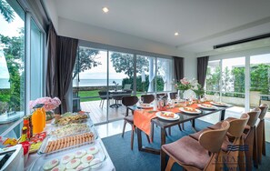 A dining area with a view of the sea, a buffet with various food items, and a table set for a meal. - Simantra Private Villas (Cha-am)