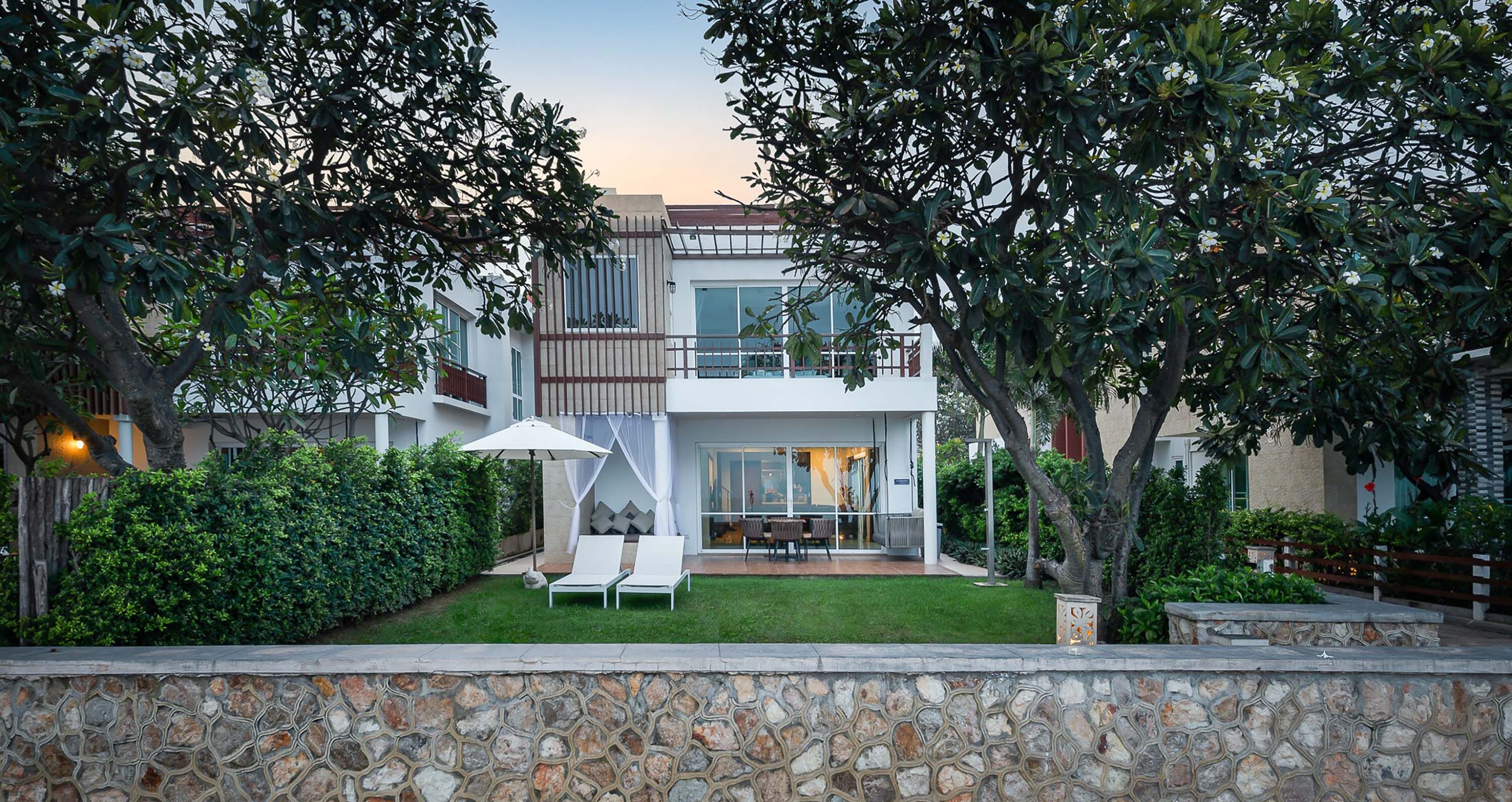 Una casa moderna de dos pisos con un muro de piedra al frente, un césped bien cuidado y un patio con muebles de exterior.