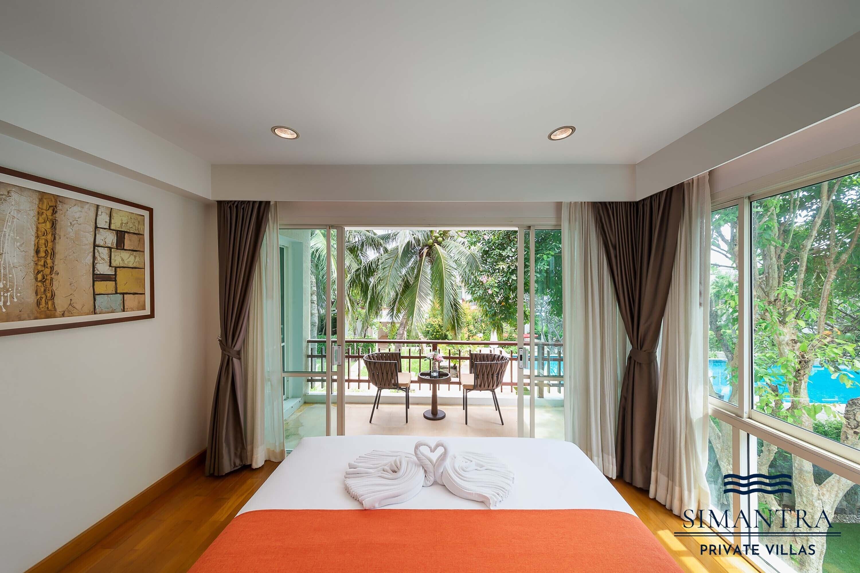 A hotel room with a large bed, a balcony with a table and chairs, and a view of greenery.