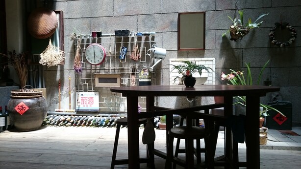 A wooden table and chairs in a courtyard with a stone wall, a clock, and various potted plants. - The Vintage Maison Tainan (Tainan)