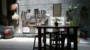 A wooden table and chairs in a courtyard with a stone wall, a clock, and various potted plants. - The Vintage Maison Tainan (Tainan)