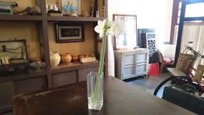 A room with a wooden table, a vase with a white flower, shelves with various items, and a bicycle in the background. - The Vintage Maison Tainan (Tainan)
