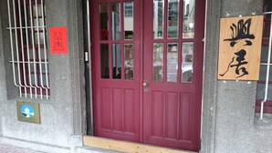 A red door with a window, a wooden sign with Chinese characters, and a small blue and white sign on the wall. - The Vintage Maison Tainan (Tainan)